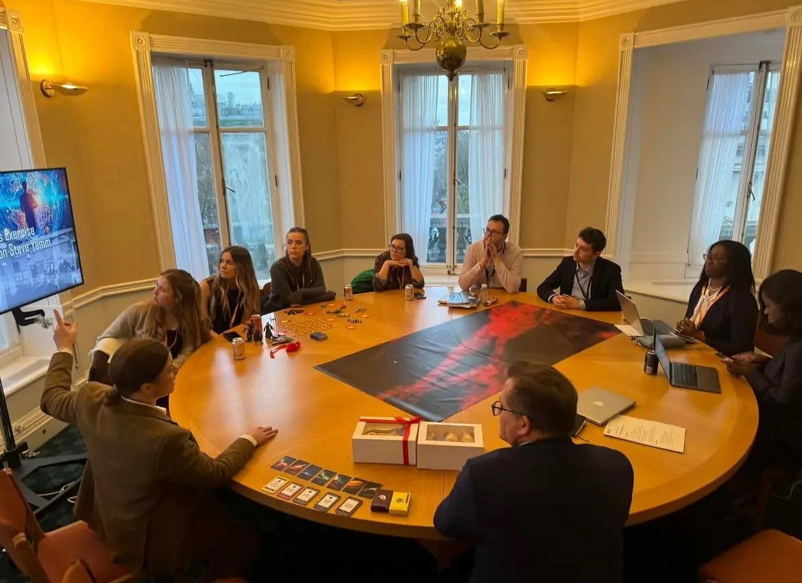 UK Government employees sat around a table listening to Michelle Richards speaking. An SOE is laid out on the table.